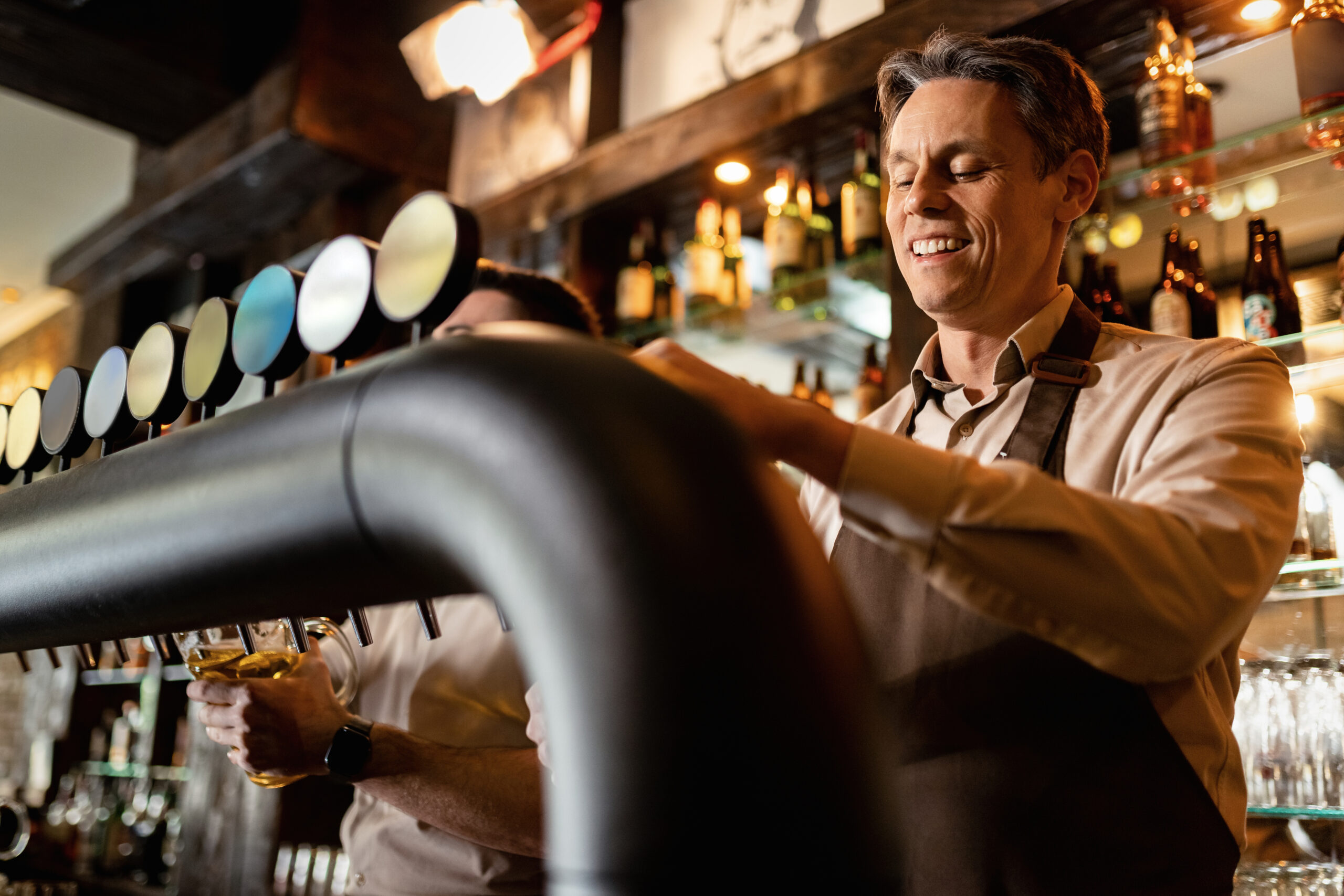Happy barista pouring draft beer while working in a pub.